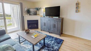 Ett vardagsrum med en soffa, ett soffbord, en öppen spis, en tv och en takfläkt.