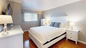 Une chambre à coucher avec un lit, des tables de chevet, une commode et une fenêtre avec des stores.