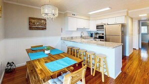 Une cuisine moderne avec des meubles blancs, un îlot central doté de tabourets, un lustre et une table à manger agrémentée de sets de table bleus.