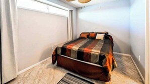 Un dormitorio con cama, ventilador de techo y piso alfombrado.