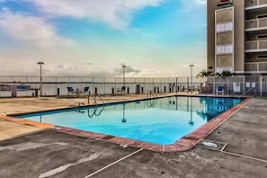 A swimming pool with a view of the ocean, a fenced deck area, and a multi-story building with balconies. - Wight Bay North 442 (Ocean City)