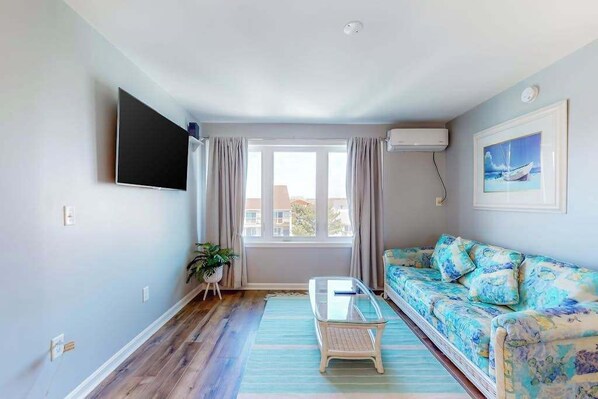 A living room with a sofa, a coffee table, a TV, and a window with curtains. - Bayshore Central 44 (Ocean City)