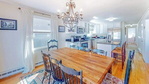 A dining area with a wooden table and chairs, a chandelier, and a kitchen in the background. - Sun-filled coastal retreat near beaches with waterfront views (Ocean City)