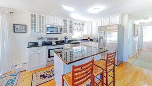 A modern kitchen with white cabinetry, a central island, and a refrigerator. - Sun-filled coastal retreat near beaches with waterfront views (Ocean City)