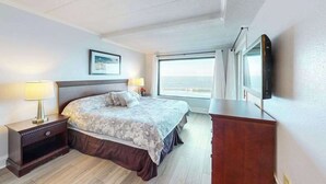 Una camera d'albergo con un letto, due abat-jour, una cassettiera, una televisione e una finestra con tende.