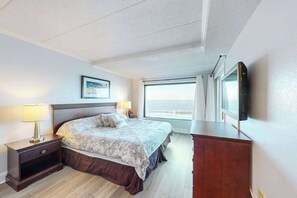 A hotel room with a bed, bedside lamps, a dresser, a TV, and a window with curtains. - Beachfront/ocean-view condo with private balconies (Ocean City)