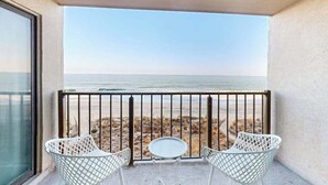Un balcone con vista sulla spiaggia, due sedie bianche e un tavolino rotondo.