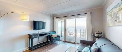 A modern living room with a flat-screen TV, a sofa, a coffee table, and a balcony with a view.
