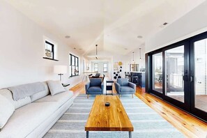 Ein modernes Wohnzimmer mit einer Couch, zwei Sesseln, einem Couchtisch und einem Essbereich mit Tisch und Stühlen.