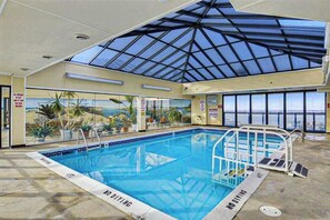 An indoor swimming pool with a glass ceiling, clear poolside area, and a view of the ocean. - Oceanfront escape with beach access, pools, sauna, tennis, & fitness room (Ocean City)