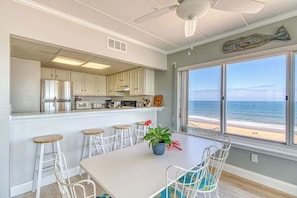 A kitchen with a view of the beach, white cabinets, a dining table with chairs, and a ceiling fan. - Bright beachfront condo with balcony, amazing views, W/D, & central AC (Ocean City)
