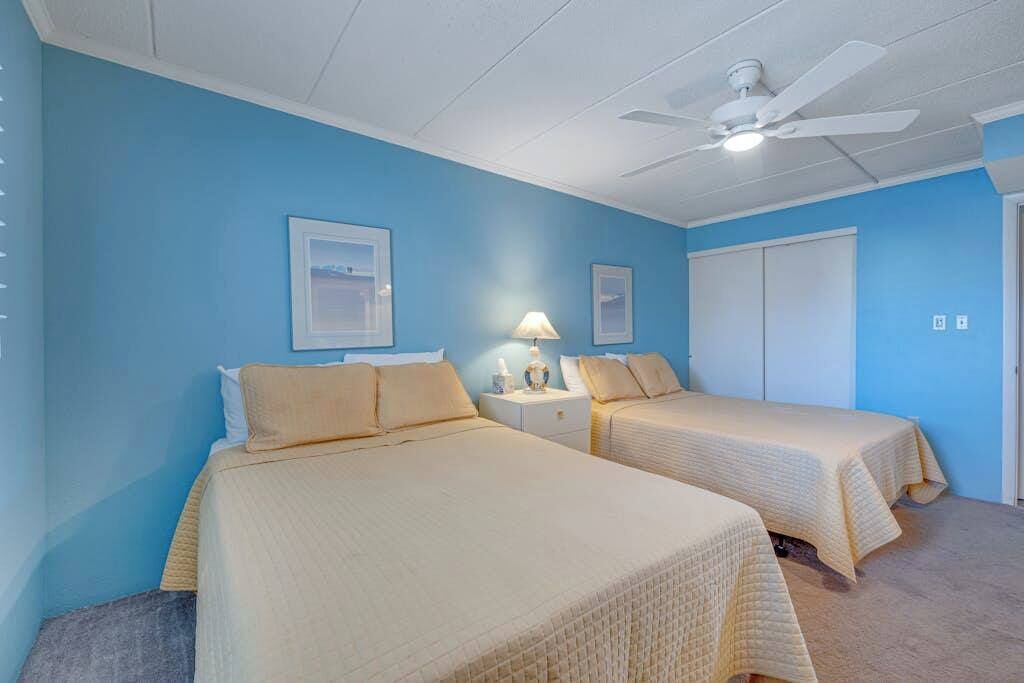 Une chambre avec deux lits, un ventilateur de plafond et une porte.