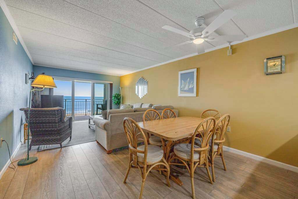 A dining area with a wooden table and chairs, a ceiling fan, and a view to the outside.