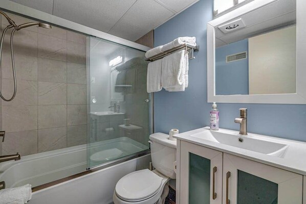 Een badkamer met een douchecabine, een wit toilet, een wastafel met spiegel en een handdoekrek.