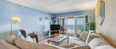 A living room with a sofa, a television, a lamp, and a balcony with a view.