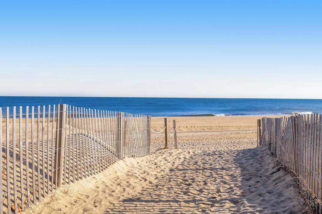 A sandy beach path leading to the ocean, bordered by wooden fences.
