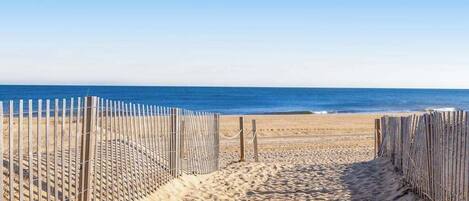 A sandy beach path leading to the ocean, bordered by wooden fences.