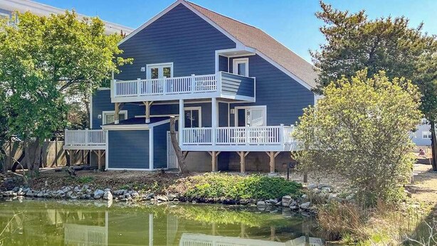 A two-story house with a balcony, a pond in front, and trees around. - Waterfront apartment w/ a furnished deck & free WiFi - walk to the beach (Ocean City)