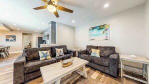 A modern living room with two sofas, a coffee table, a ceiling fan, and a painting of a beach scene. - Waterfront apartment w/ a furnished deck & free WiFi - walk to the beach (Ocean City)