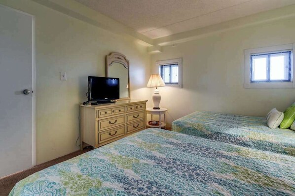 Un dormitorio con dos camas, un aparador, un televisor, una lámpara y una ventana.