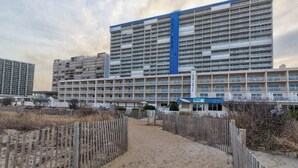 Et stort hotel med flere etager og balkoner, en sti af sand der fører til indgangen, og et træhegn omkring ejendommen.