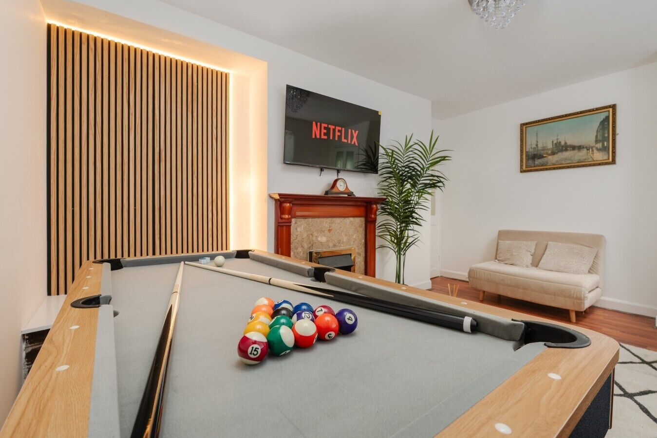 A pool table with balls, a sofa, a fireplace, a plant, and a TV displaying 'NETFLIX'.