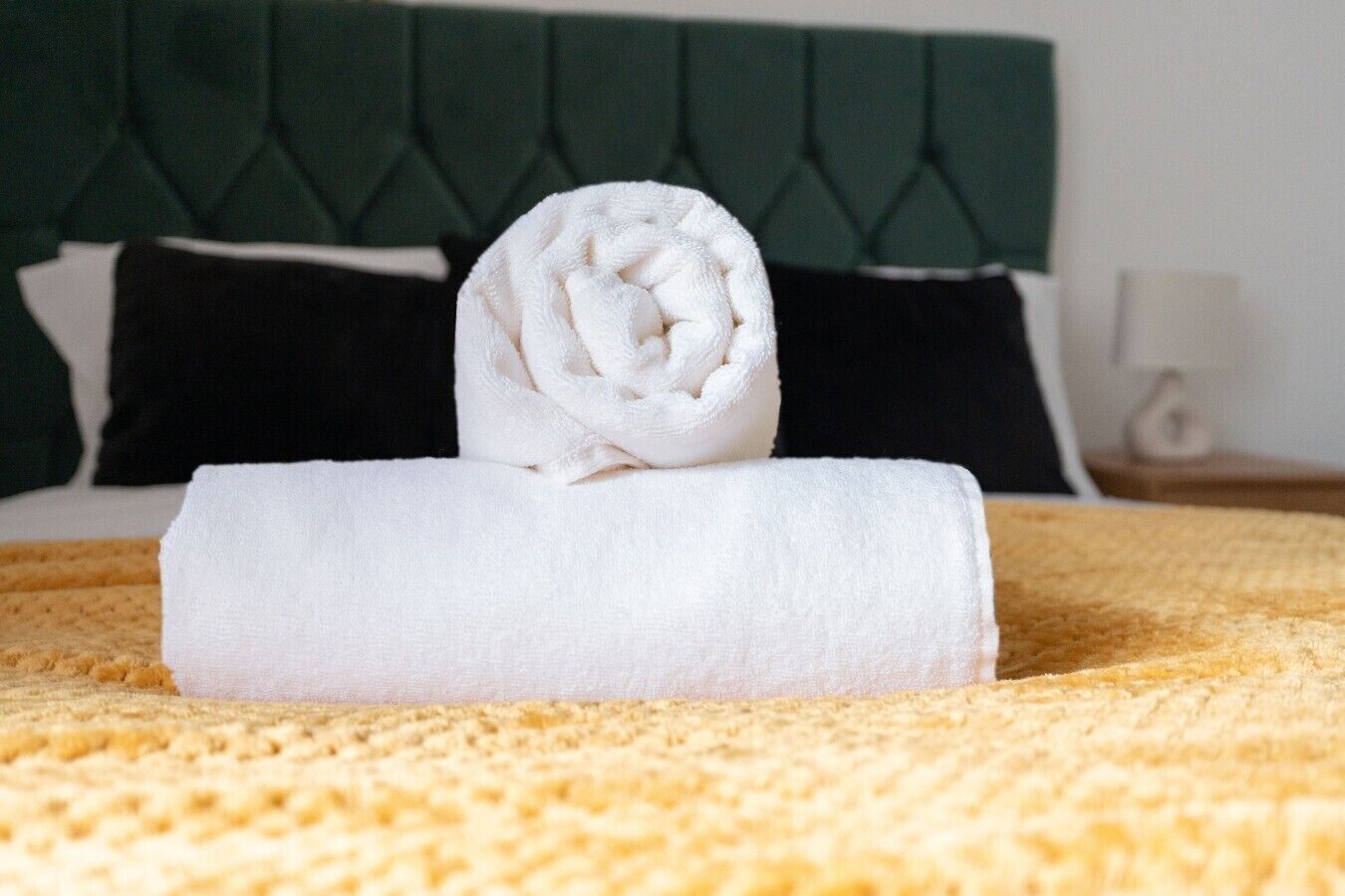 Cama bem arrumada com uma toalha enrolada e um cobertor dobrado.