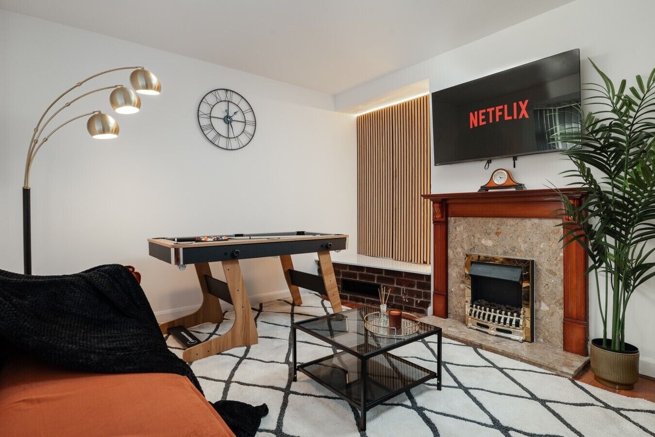 A modern living room with a pool table, a fireplace, a TV mounted on the wall, and a clock.