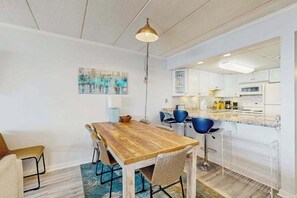 Un comedor con una mesa y sillas de madera, una lámpara colgante y una cocina al fondo.