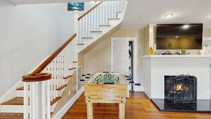 A living room with a wooden foosball table, a fireplace, a TV, and a staircase. - Boardwalk Bungalow (Ocean City)
