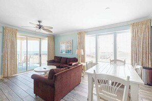 A room with a sofa, a dining table with chairs, a ceiling fan, and large windows with curtains. - Belmont Towers 601 (Ocean City)