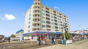 Un hotel de varios pisos con balcones, un paseo marítimo frente al edificio y una tienda de dulces.