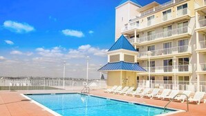 Una piscina con tumbonas, un edificio con balcones y un cielo despejado.