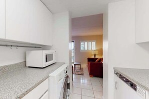A compact kitchen with a microwave, washing machine, and a small table. - Sixth-floor oceanfront condo w/central AC, washer/dryer, furnished balcony (Ocean City)