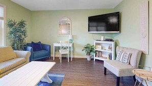 A living room with a sofa, a coffee table, a TV, a bookshelf, and a potted plant. - Sunset Drive townhouse with WiFi, private W/D & central AC - dog-friendly (Ocean City)