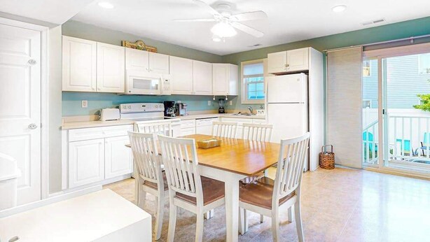 A kitchen with white cabinets, a wooden dining table, and chairs. - Sunset Drive townhouse with WiFi, private W/D & central AC - dog-friendly (Ocean City)