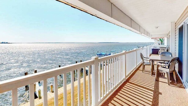 Varanda com vista para o mar, uma mesa com cadeiras e um corrimão branco.