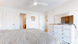 Quarto com cama, penteadeira, ventoinha no teto e porta de acesso a outro espaço.
