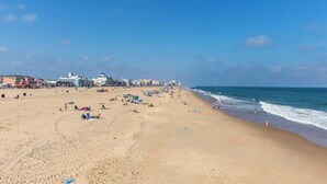 Uma extensa praia de areia com pessoas, guarda-sóis e edifícios ao fundo.