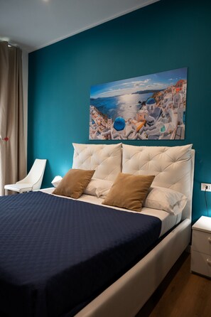 A bedroom with a bed, a nightstand, a chair, and a painting on the wall. - Hotiday Relais di Gusto (La Spezia)