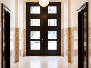 Un corridoio con una porta in legno scuro dotata di diversi pannelli di vetro, che conduce a un ambiente ben illuminato.