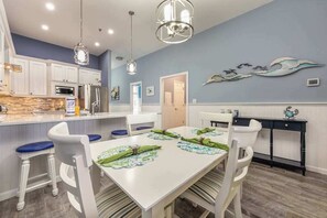 A modern kitchen with white cabinets, a built-in oven, and a dining area with a white table and blue chairs. - Harbour Club A9 (Ocean City)