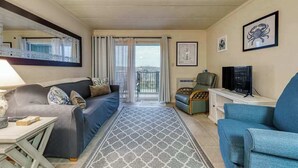 A living room with a sofa, a blue armchair, a TV, a small table, and a patterned rug. - Constellation House 107 (Ocean City)