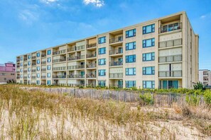 Ein mehrstöckiges Hotel mit Balkonen, einem Sandstrand davor und einem klaren Himmel.