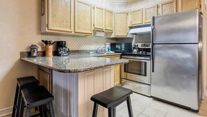 A kitchen with wooden cabinets, a stainless steel refrigerator, a microwave, and a coffee maker. - Constellation House 107 (Ocean City)