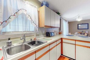 A kitchen with a sink, wooden cabinets, a toaster, and a window with curtains. - Comfy & Well-Appointed Home in Oceanside Building w/Free WiFi, Central AC (Ocean City)