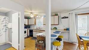 A compact kitchen with a dining area, featuring a small table, bar stools, and a view of the balcony. - Alexandra 103 (Ocean City)