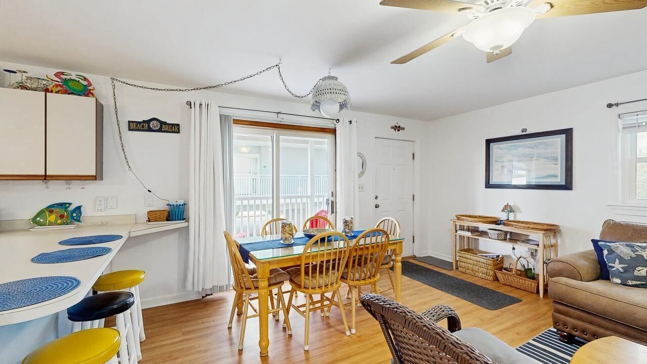 A dining area with a wooden table and chairs, a kitchen with white cabinets, and a living area with a sofa and a framed picture on the wall.