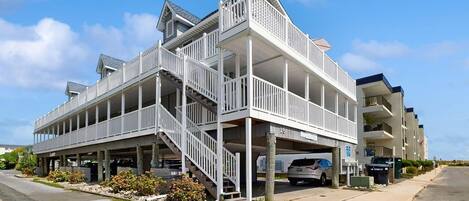 A multi-story building with a balcony on the upper floor, a covered parking area, and a clear sky.