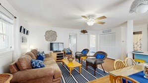 Ein Wohnzimmer mit einer Couch, Sesseln, einem Fernseher und einem Esstisch.